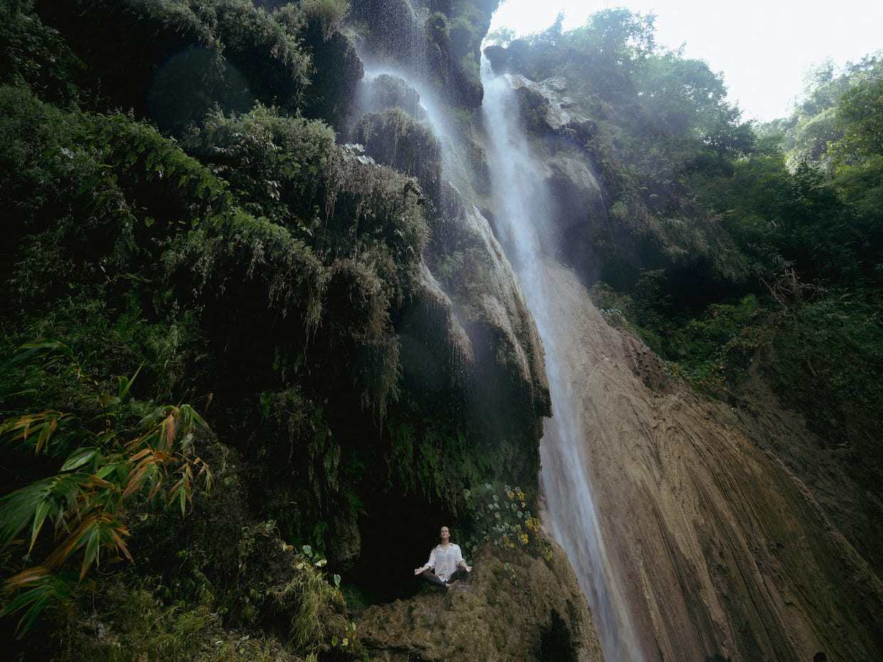 Guest meditating in lotus pose at Himalayan waterfall near Rishikesh