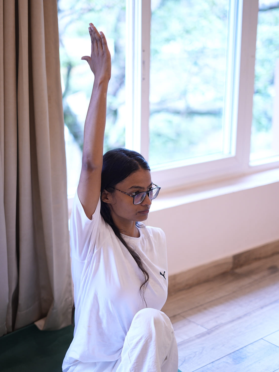Retreat student in seated arm-raised yoga pose by window