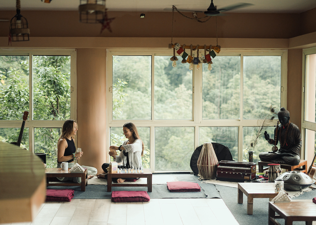 Two students share quiet conversation over chai in the warm cliff-edge café at Rishikesh Yogpeeth
