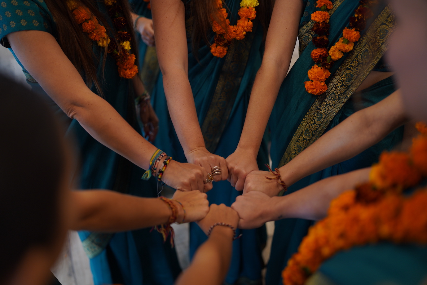Circle of fists from a graduating class of female students in teal saris and orange garlands
