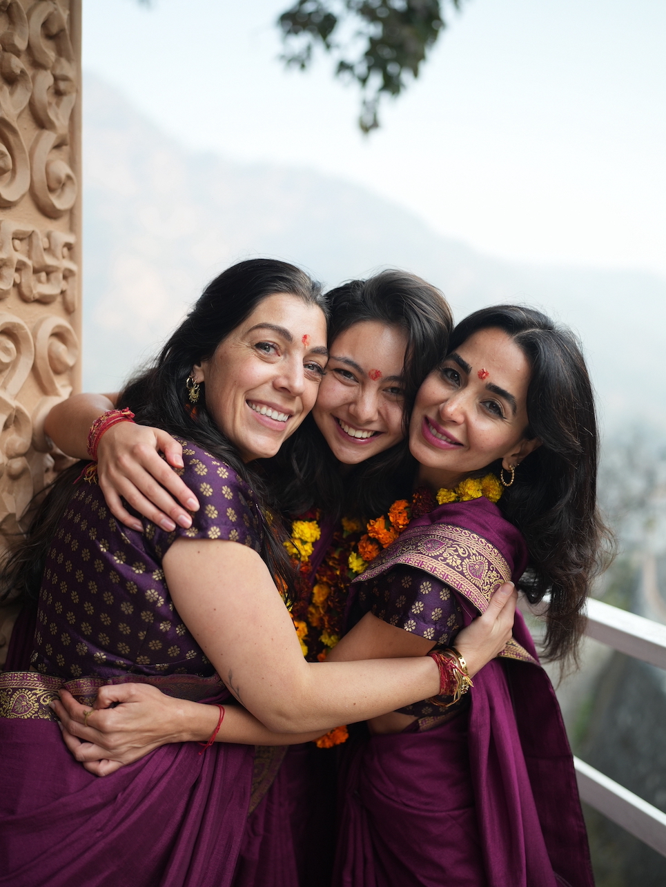 Three female graduates from different countries embracing in traditional purple saris on certification day