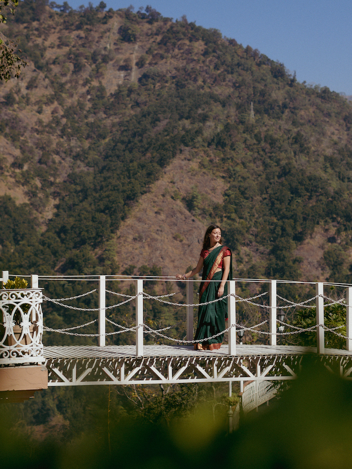A student in green sari pauses on the iconic white footbridge with the dramatic Himalayan mountains behind her